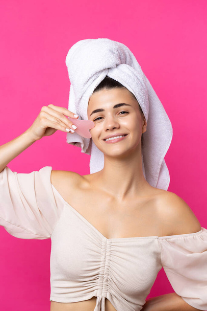Красивая веселая привлекательная девушка с полотенцем на голове держит косметический камень в сердце рядом с ее лицом. - Фото, изображение