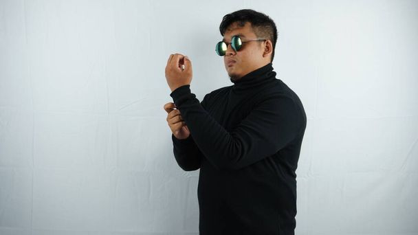 Nuori mies valkoisessa paidassa lasit ja musta huppari poseeraa harmaalla taustalla - Valokuva, kuva