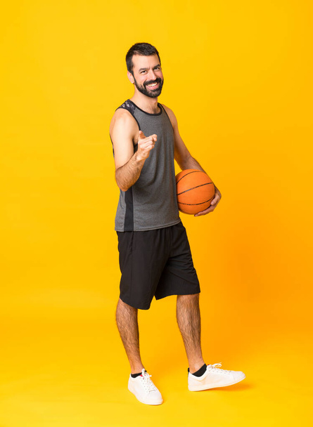 Ganzkörperaufnahme eines Mannes auf isoliertem gelben Hintergrund, der Basketball spielt und nach vorne zeigt - Foto, Bild