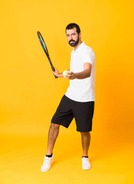 Full-length shot of man over isolated yellow background playing tennis - Photo, Image