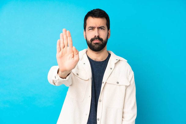 Junger gutaussehender Mann mit weißer Cordjacke über isoliertem blauem Hintergrund macht Stop-Geste - Foto, Bild