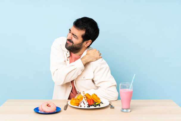 Человек за столом, завтракающий вафлями и молочный коктейль, страдающий от боли в плече за то, что сделал усилие - Фото, изображение