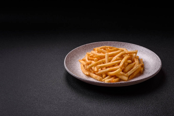 Delicious crispy golden fries with salt and spices on a dark concrete background - Photo, Image