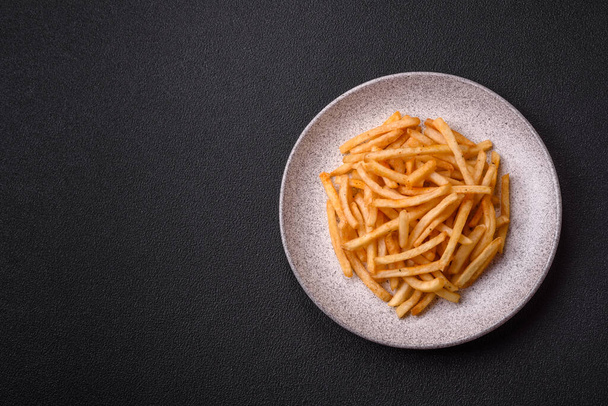 Delicious crispy golden fries with salt and spices on a dark concrete background - Photo, Image