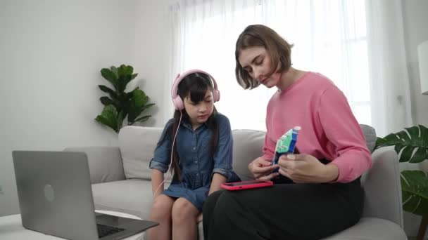 Menina bonito asiático ouvir música do laptop usando fone de ouvido, enquanto a mãe adorável tocando ukulele enquanto ensina a filha jovem tocando música acústica. Aprendizado bonito da criança sobre instrumento. A pedagogia. - Filmagem, Vídeo