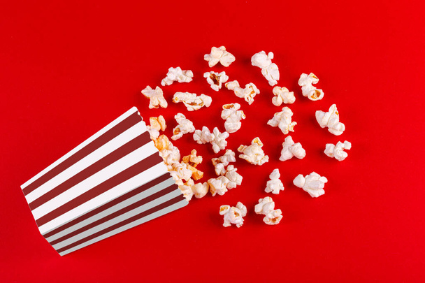 doos met popcorn gestreept in verschillende kleuren op een rode achtergrond close-up - Foto, afbeelding