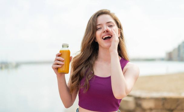 jong roodharig meisje houden een sinaasappelsap in de buitenlucht schreeuwen met mond wijd open - Foto, afbeelding