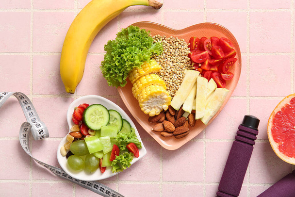 Тарелки со свежими здоровыми продуктами и измерительной лентой на розовом фоне плитки. Концепция питания - Фото, изображение
