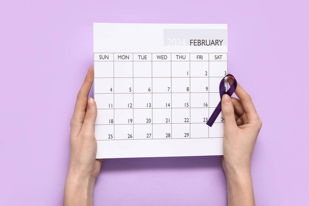 紫色の背景にリボンと紙のカレンダーを意識した女性の手. がんコンセプト - 写真・画像
