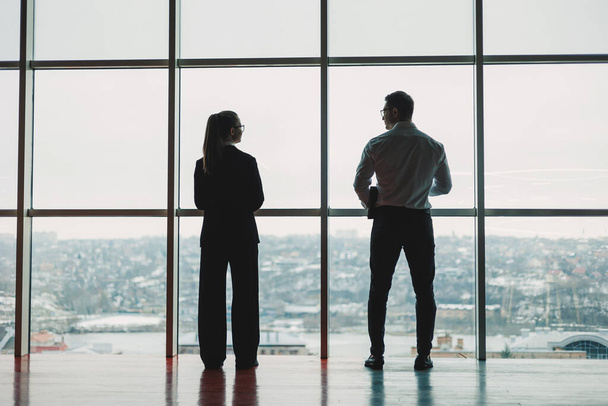 大きなパノラマの窓の背景に男女がオフィスに立っている. 従業員との現代的な広々としたワークスペース. ビジネスパートナー - 写真・画像