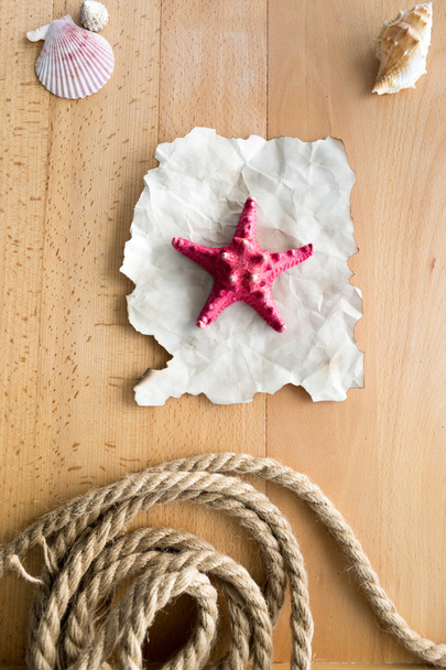 Red starfish lying on piece of old paper on wooden planks - Photo, Image