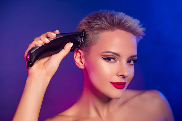 Крупним планом фото дівчини, що ріже волосся з професійним електричним машинним затискачем над туманним неоновим ультрафіолетовим фоном. - Фото, зображення