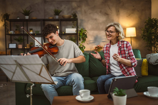 Young man learn how to play violin under instruction of mature woman female professor tutor at home take private class - Foto, Imagen