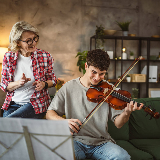 Jongeman leren hoe om viool te spelen onder instructie van volwassen vrouw vrouwelijke professor tutor thuis nemen prive-les - Foto, afbeelding