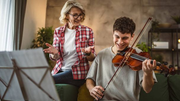 Młody mężczyzna nauczyć się grać na skrzypcach pod okiem dojrzałej kobiety profesor korepetytor w domu wziąć prywatne zajęcia - Zdjęcie, obraz