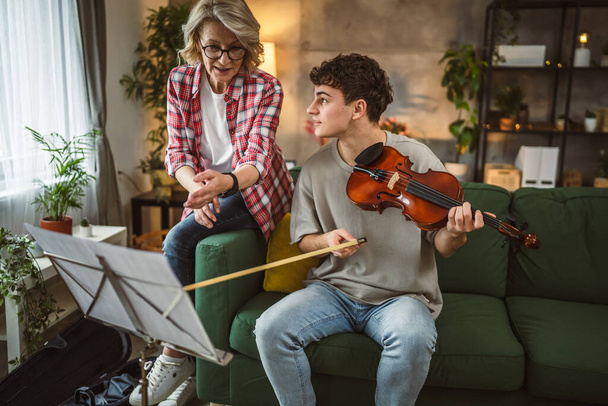 Молодой человек учится играть на скрипке под руководством зрелой женщины-преподавателя дома взять частный класс - Фото, изображение