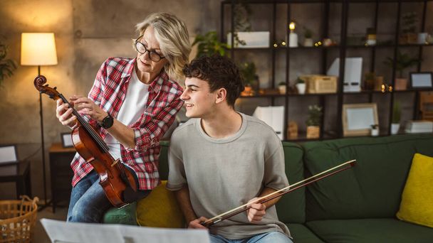 Hombre joven aprender a tocar el violín bajo la instrucción de la mujer madura profesora tutor en casa tomar clases privadas - Foto, Imagen