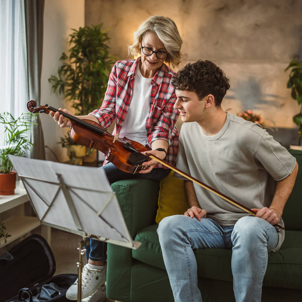 Νεαρός άνδρας να μάθουν πώς να παίζουν βιολί, υπό την καθοδήγηση της ώριμης γυναίκας γυναίκα καθηγητής δάσκαλος στο σπίτι να λάβει ιδιωτική τάξη - Φωτογραφία, εικόνα