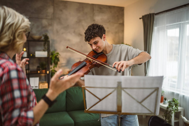 Молодий чоловік навчиться грати на скрипці під інструкцією зрілої жінки, вчителька-професорка вдома бере приватний клас - Фото, зображення