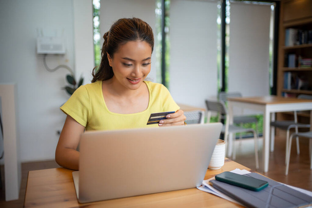 Donna asiatica seduta e in possesso di carta di credito per lo shopping online da laptop e smartphone a casa. - Foto, immagini