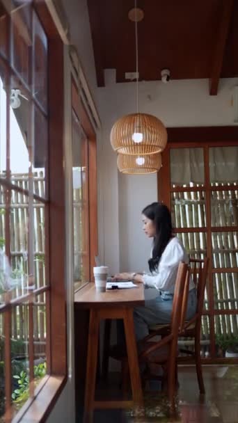Asijská mladá obchodnice pracuje v nedaleké kavárně a používá svůj notebook. Vysoce kvalitní 4K záběry - Záběry, video