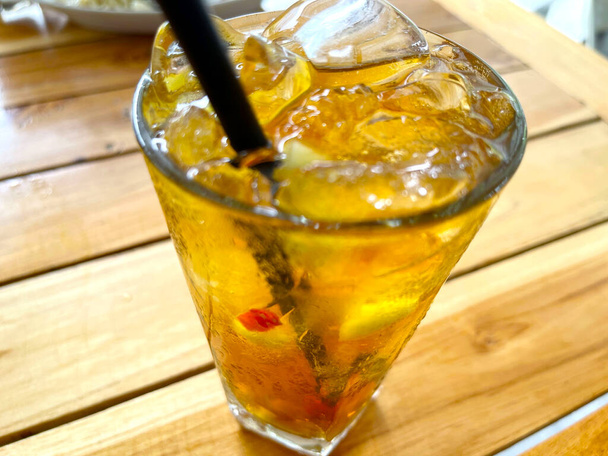 świeży koktajl owocowy napój alkoholowy z rumem i whisky w przezroczystej szklance i kawałek lodu na drewnianym tle stołu - Zdjęcie, obraz