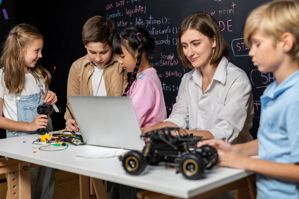 Lerarencodering om kinderen te laten zien hoe ze robots moeten coderen in de STEM-klasse. Kinderen leuk om te zien hoe leraar coderen met zelfverzekerde enige jongen in blauw shirt het nemen van nota met serieuze blik. Erutie. - Foto, afbeelding