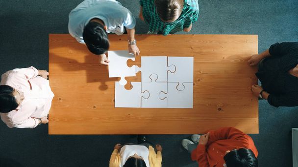 Blick von oben auf qualifizierte Geschäftsleute montieren Puzzle auf Besprechungstisch. Gruppe verschiedener Teams, die zusammenarbeiten, um das Rätsel zu lösen. Stellvertretend für Einheit, Zusammenhalt, Kooperation. Einberufung. - Foto, Bild