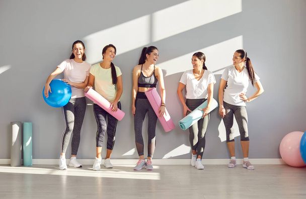 Group of young sporty girls, attractive slim happy people posing in fitness club, sportswomen team holding yoga mats. Active friends exercise or sport instruction, recreational activity together  - Foto, Bild