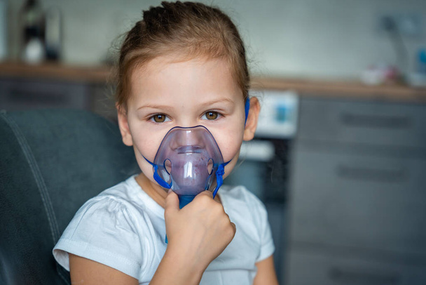 Linda niña está sentada y sosteniendo una máscara de nebulizador apoyado en la cara, concepto de tratamiento de las vías respiratorias. Foto de alta calidad - Foto, imagen