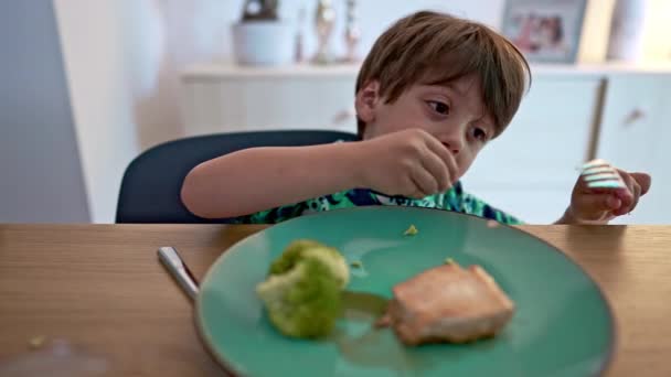 Мальчик сидит за столом и ест рыбу вилкой - голубая тарелка, лосось и брокколи - Кадры, видео