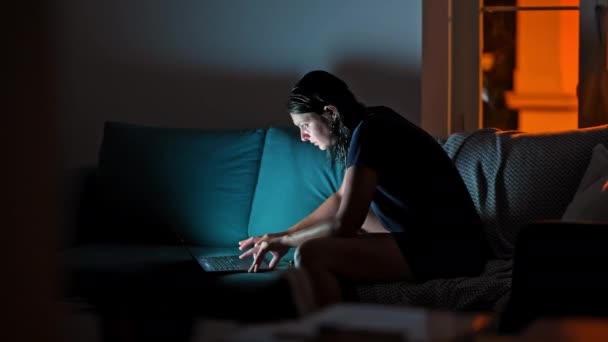 Night Time Computing - Žena na pohovce s notebookem a sluchátky v matné knihovně. Žena procházení internetu ve večerních hodinách, v přední části obrazovky - Záběry, video