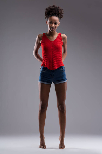 Con confianza de pie, la joven con una camiseta roja y pantalones cortos de mezclilla muestra una mezcla de fuerza y gracia - Foto, Imagen