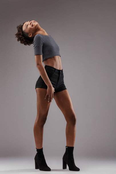 Top listrado e calções pretos usados por esticar mulher, cujo penteado afro dança com seu movimento - Foto, Imagem