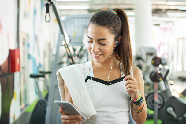 Retrato de mujer atlética escuchando música en un smartphone en un gimnasio - Foto, Imagen