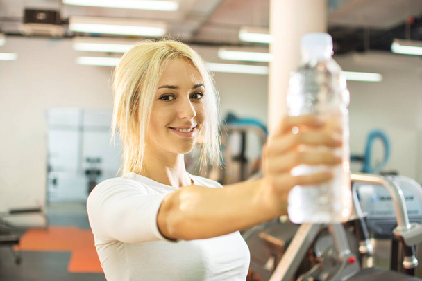 Young blonde woman showing bottle of water in a gym. - Photo, Image