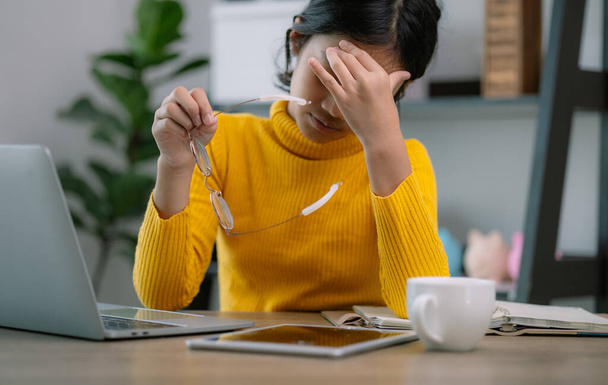 Kobieta w żółtym swetrze siedzi przy biurku z laptopem i tabletem. Trzyma okulary i jest w stanie stresu. - Zdjęcie, obraz