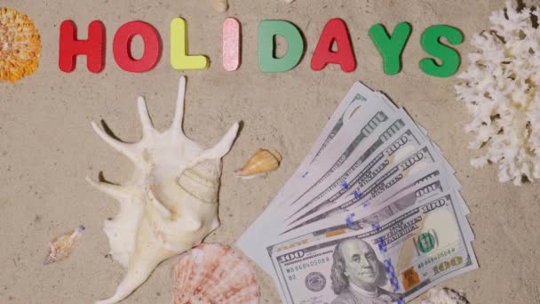 Гроші на свята, відпустку, вихідні. Добре заслужений відпочинок на дорогому приморському курорті. Долари на піску пляжу. Напис на піску "свята" - Кадри, відео