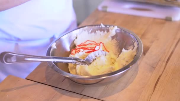 Les mains des enfants remuent diligemment la coloration des aliments rouges dans le glaçage à la crème au beurre pendant un cours de cuisine, une partie animée d'une célébration d'anniversaire. Le bol en acier inoxydable sur la table en bois est le - Séquence, vidéo
