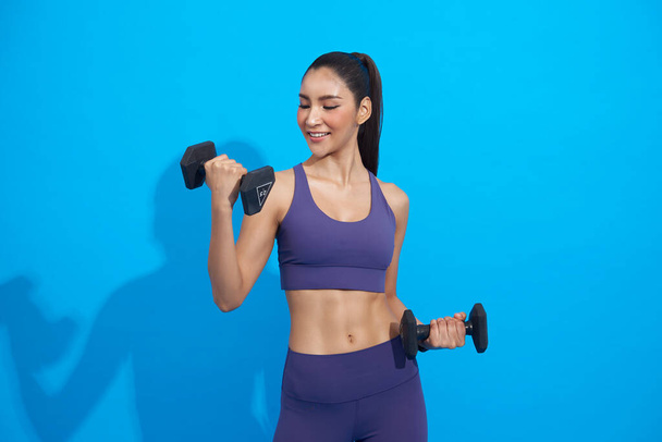 Gesunde junge asiatische sportliche Mädchen machen Übungen mit Kurzhanteln isoliert auf blauem Fitness-Studio Hintergrund. - Foto, Bild