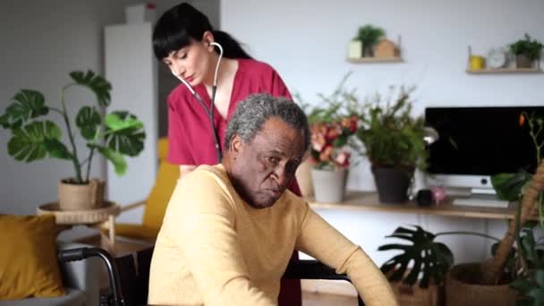 Verpleegster neigt naar oudere man die thuis last heeft van rugpijn, als voorbeeld van persoonlijke gezondheidszorg. - Video