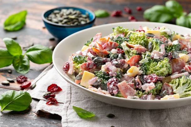 Gesunder hausgemachter Brokkoli-Salat mit Speck, roten Zwiebeln, Preiselbeeren, Kürbiskernen und Käse. - Foto, Bild