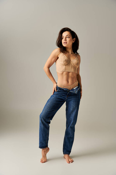 Una giovane donna colpisce una posa afosa in un reggiseno e jeans. - Foto, immagini
