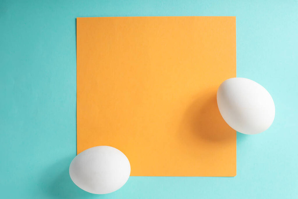 Zwei weiße Eier mit gelber Karte auf blauem Hintergrund. Ansicht von oben - Foto, Bild