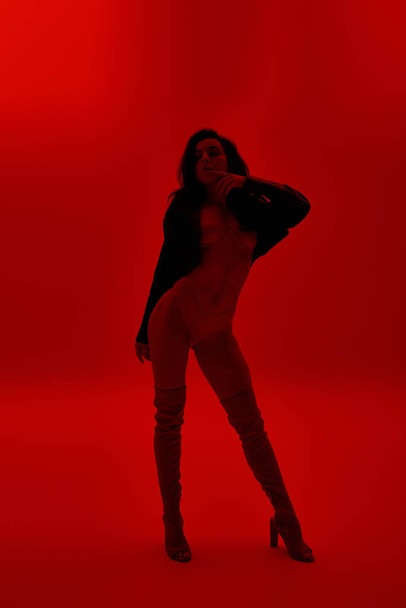 Eine junge Frau posiert verführerisch vor leuchtend rotem Hintergrund. - Foto, Bild