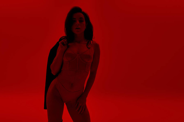 Mujer de pie en una habitación roja con chaqueta en la espalda. - Foto, imagen