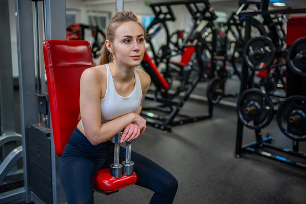 Jeune femme posant avec des haltères dans ses mains et s'entraîne dans la salle de gym effectuant un exercice. Photo de haute qualité - Photo, image