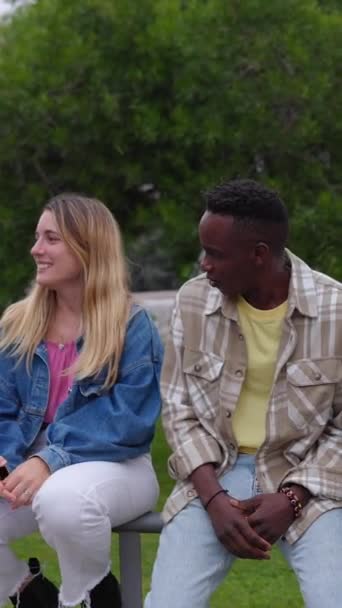 Multiracial joven hombre y mujer riendo mientras pasa el rato con amigos al aire libre. Adolescentes despreocupados riendo juntos disfrutando del tiempo en la ciudad. Vídeo de pantalla HD vertical. - Metraje, vídeo