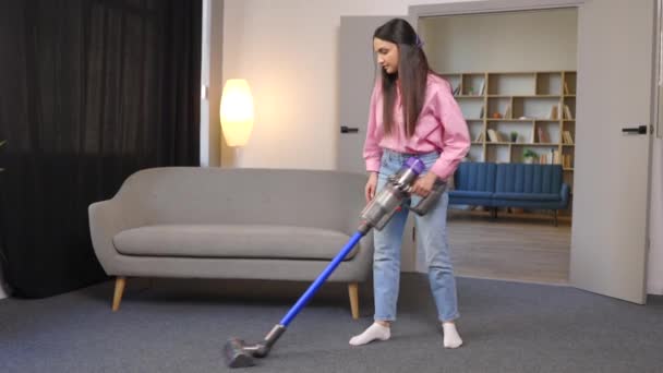 La giovane donna usa l'aspirapolvere a batteria per pulire il tappeto di casa. Moderna pulizia facile - Filmati, video