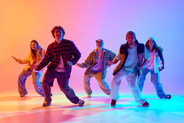 Talented young people, friends in motion, dancing hip hop, training against gradient studio background in neon light. Concept of modern dance style, hobby, active lifestyle, youth culture - Photo, Image